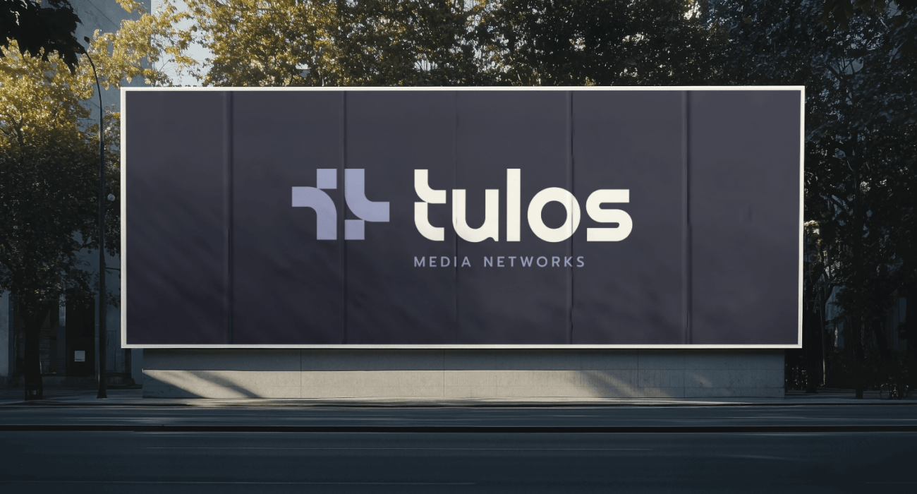 Sidewalk billboard depicting the Tulos logo on dark gray purple background.